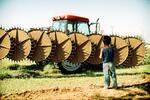Young Migrant Boy Stands Before Lethal Farm Equipment