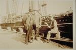 Three men on wharf beside whaling schooner John R. Manta